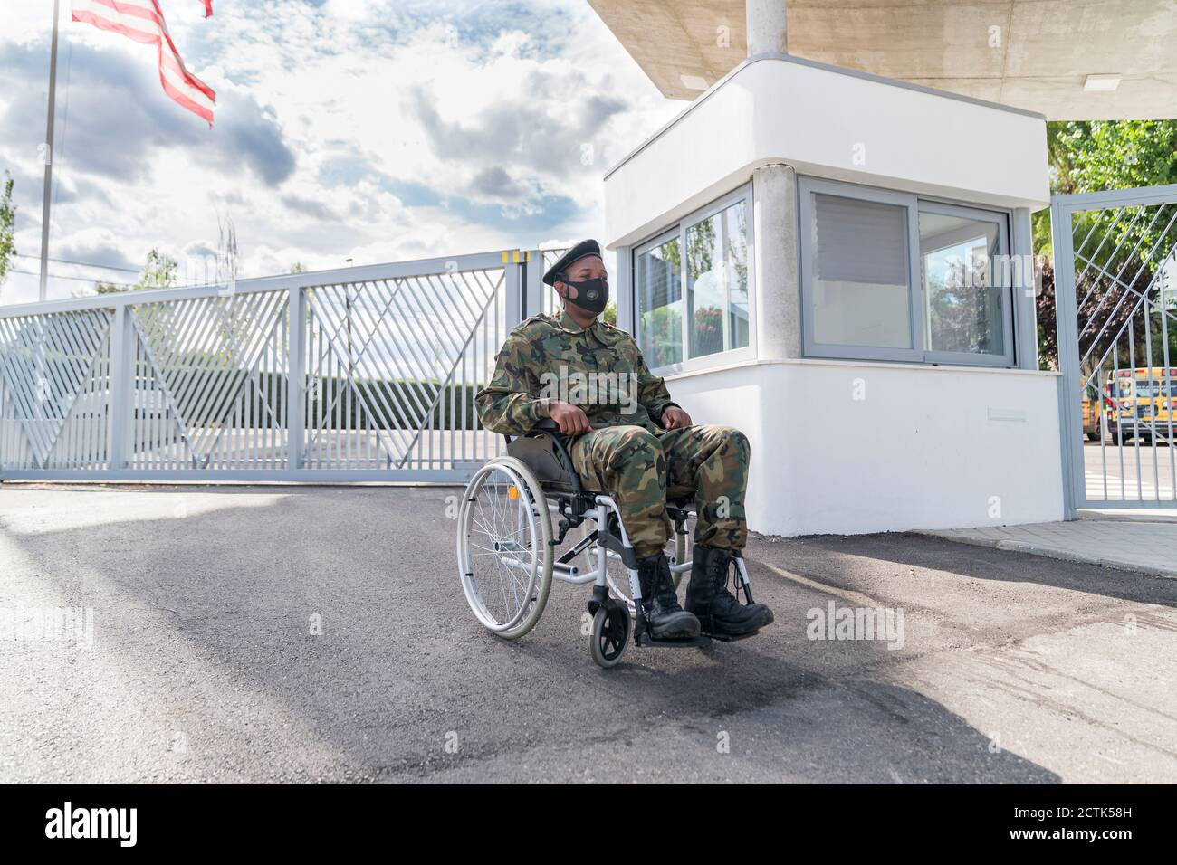 Army soldier with protective face mask sitting on wheelchair against cloudy sky Stock Photo