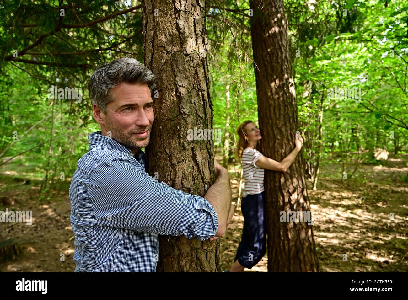 Man and woman hugging tree while standing in forest Stock Photo - Alamy