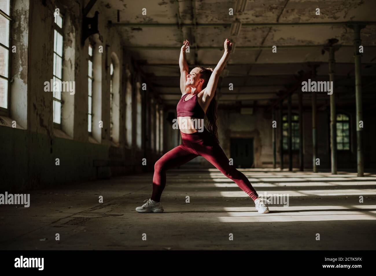Smiling woman doing crescent lunge exercising at abandoned factory Stock Photo