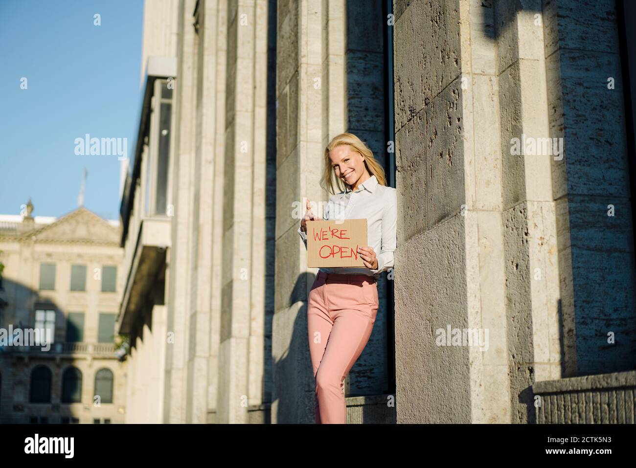 Smiling female professional holding open sign cardboard placard by building in financial district Stock Photo