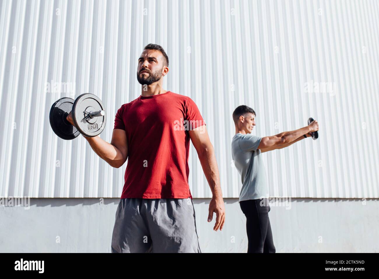 Young athletes exercising with sports equipment while standing against wall Stock Photo