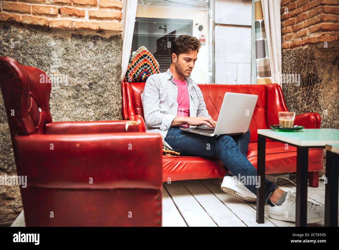 Mid adult man using laptop while sitting on sofa in coffee shop Stock Photo