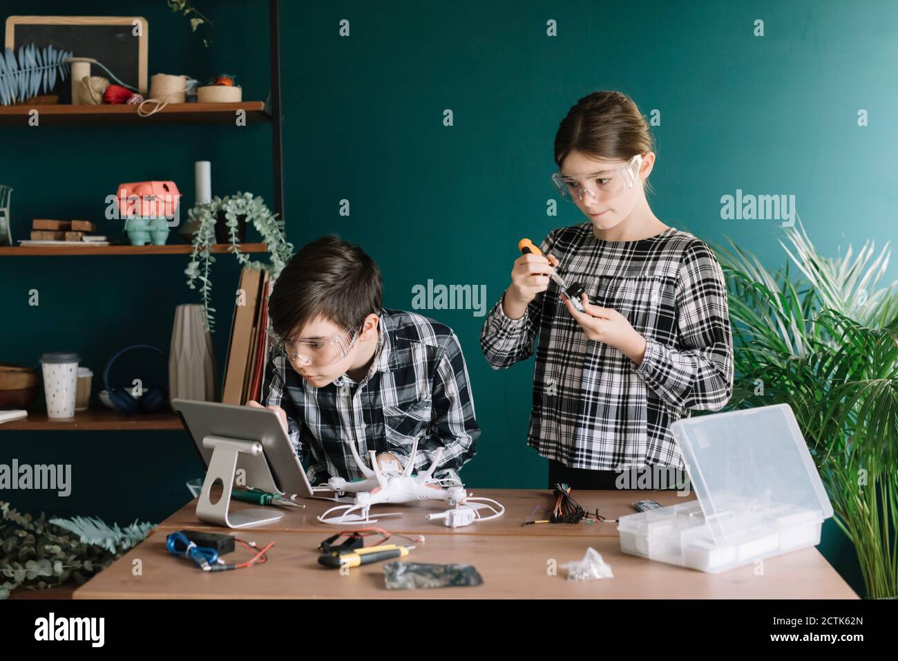 Siblings using digital tablet while preparing drone on table against wall at home Stock Photo