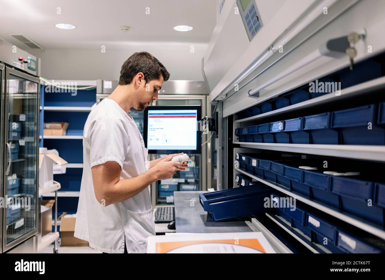 Male doctor holding medicine bottle while standing at table in pharmacy Stock Photo