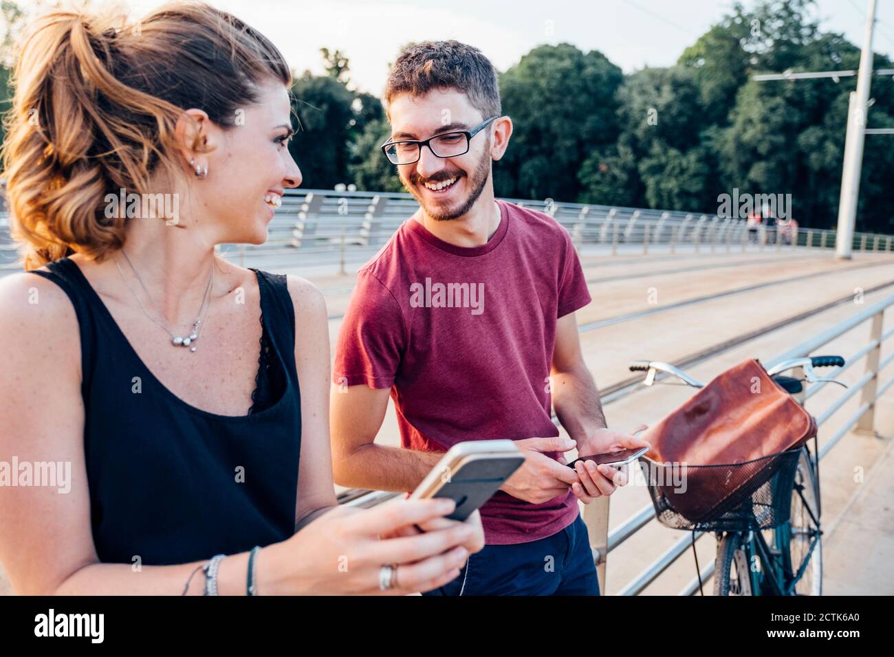 Happy couple using smart phones while standing on bridge at sunset Stock Photo