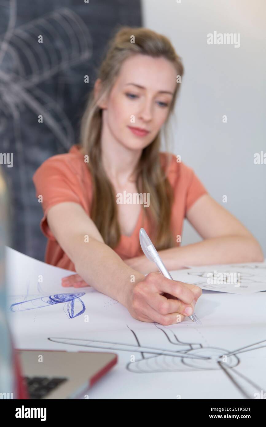 Woman working on drawing of wind turbine model at desk in home office Stock Photo