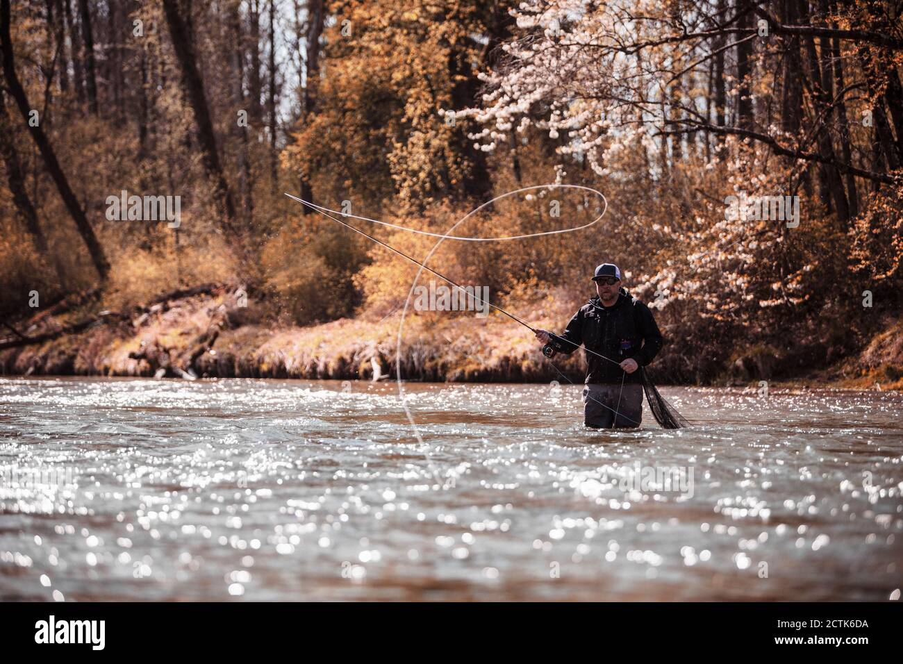 Fly Fisherman casting fishing line while standing in river at forest Stock Photo