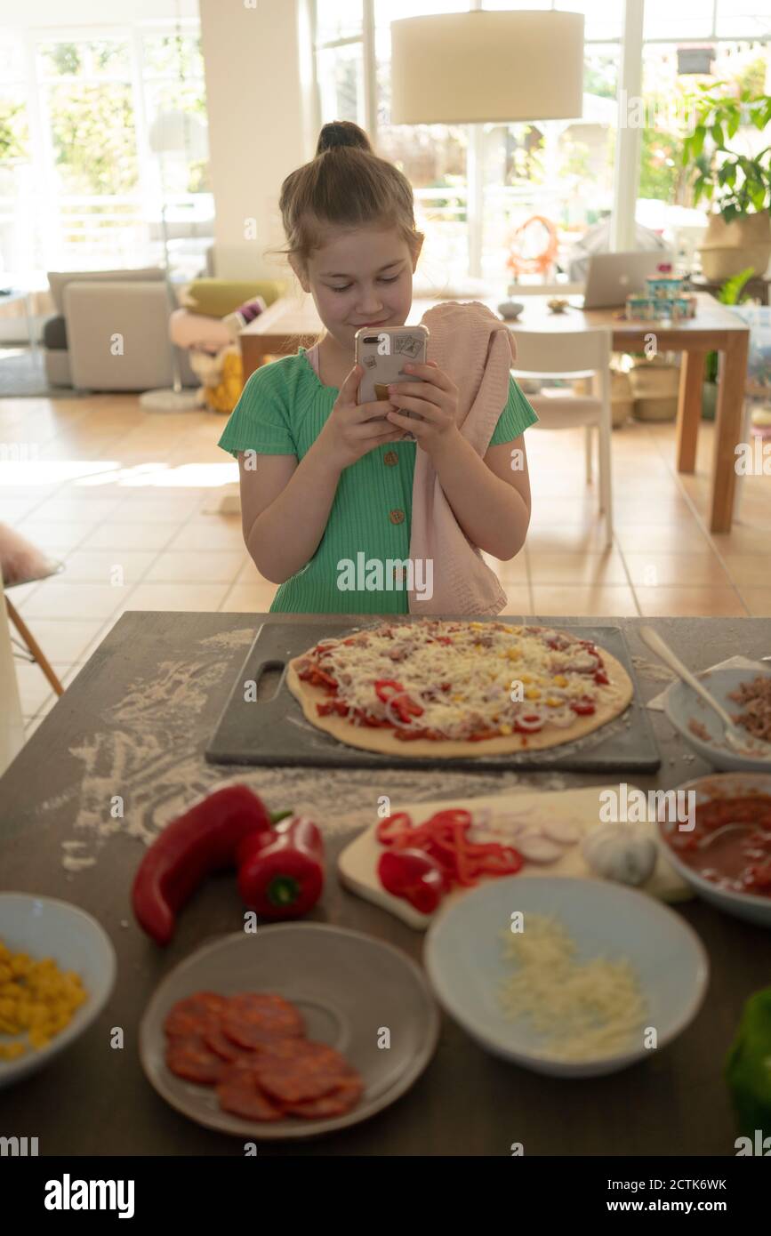 Girl photographing pizza over kitchen island Stock Photo