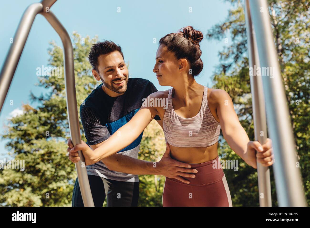 Man supporting woman doing press-ups on a fitness trail Stock Photo