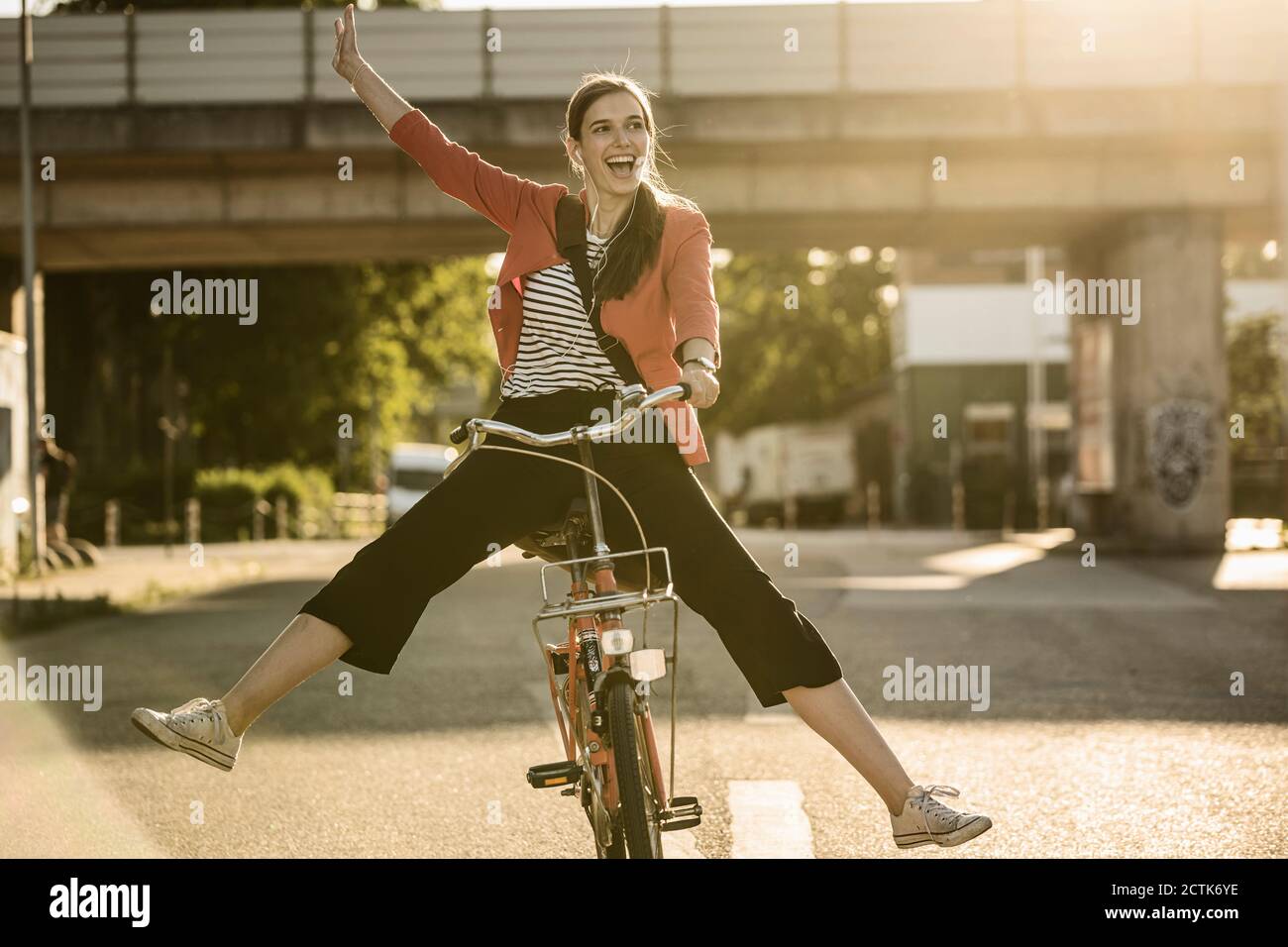 Cheerful woman enjoying cycling on street in city during sunny day Stock Photo