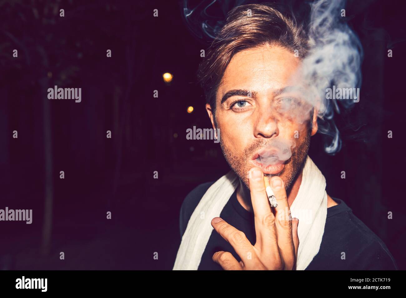Close-up of handsome man smoking cigarette outdoors at night Stock Photo