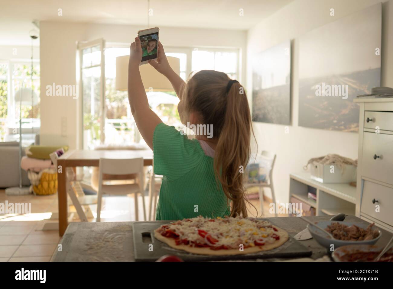 Girl taking selfie with pizza on kitchen island at home Stock Photo