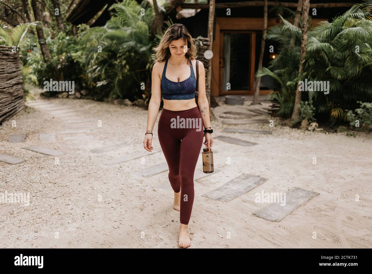 Smiling woman with bottle walking on sand Stock Photo