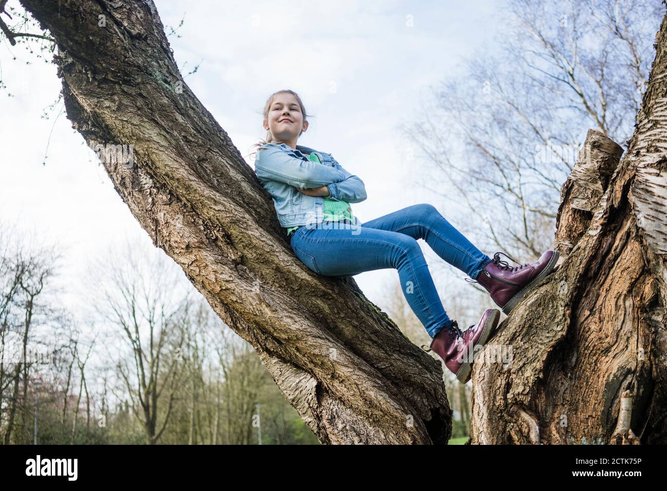 Smiling girl with arms crossed leaning on tree trunk in park Stock Photo
