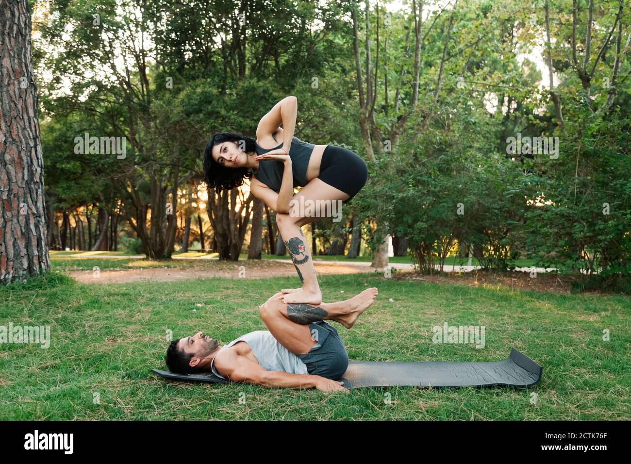 Man balancing girlfriend on legs while practicing acroyoga in public park Stock Photo