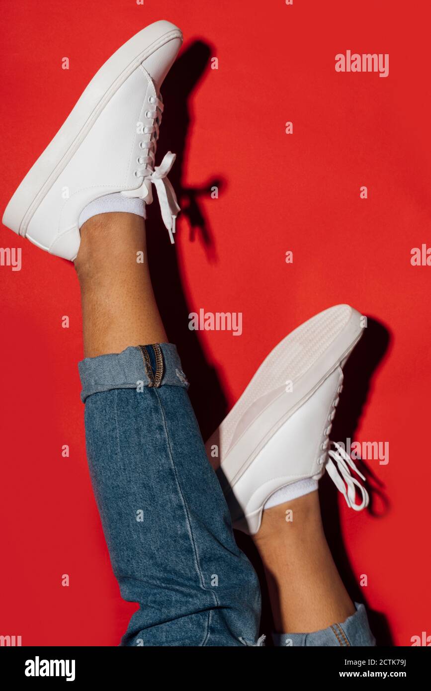 Close-up of woman wearing sneakers with feet up on red background Stock Photo