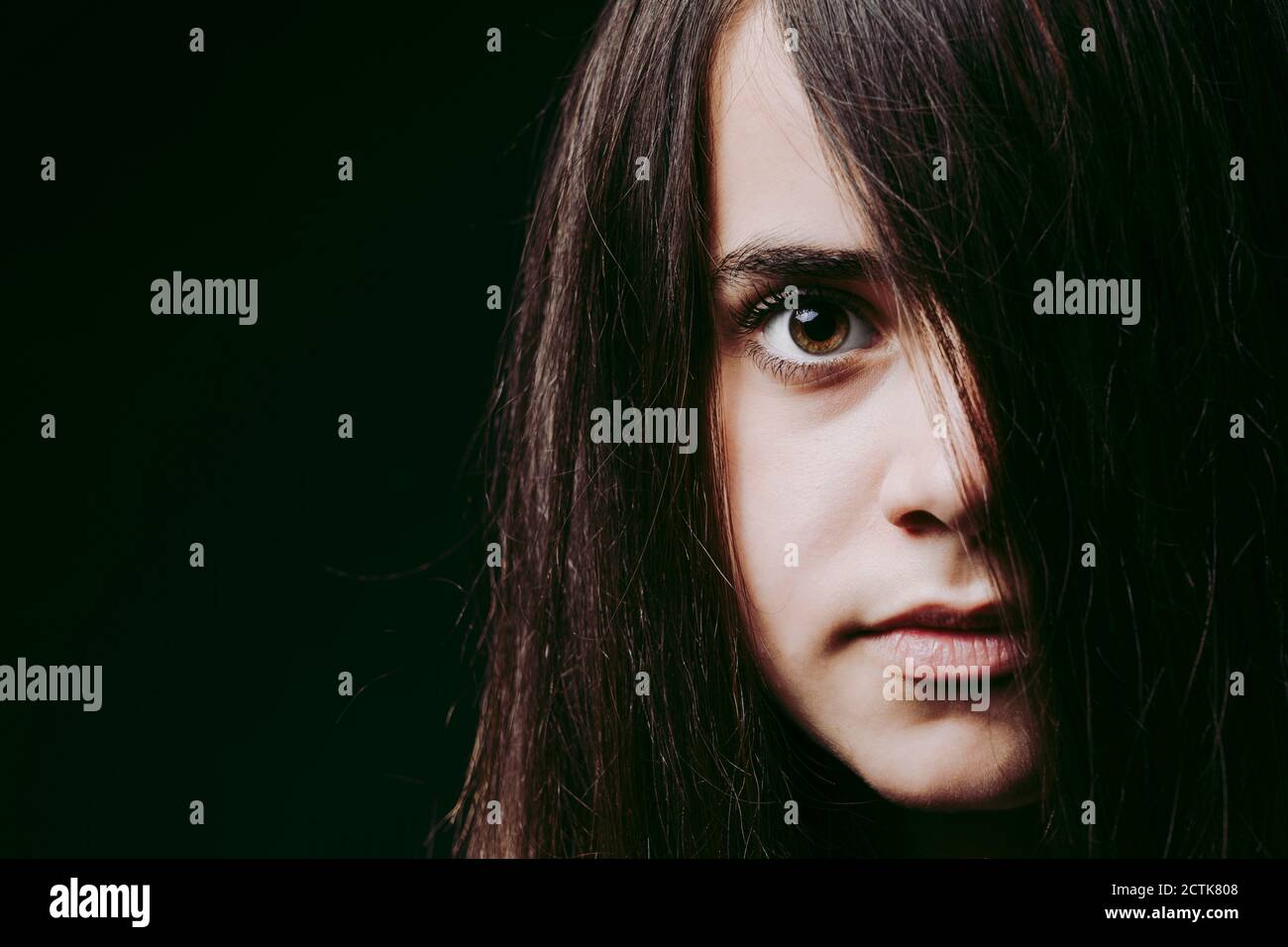 Close-up of girl with long brown hair on face against black background Stock Photo