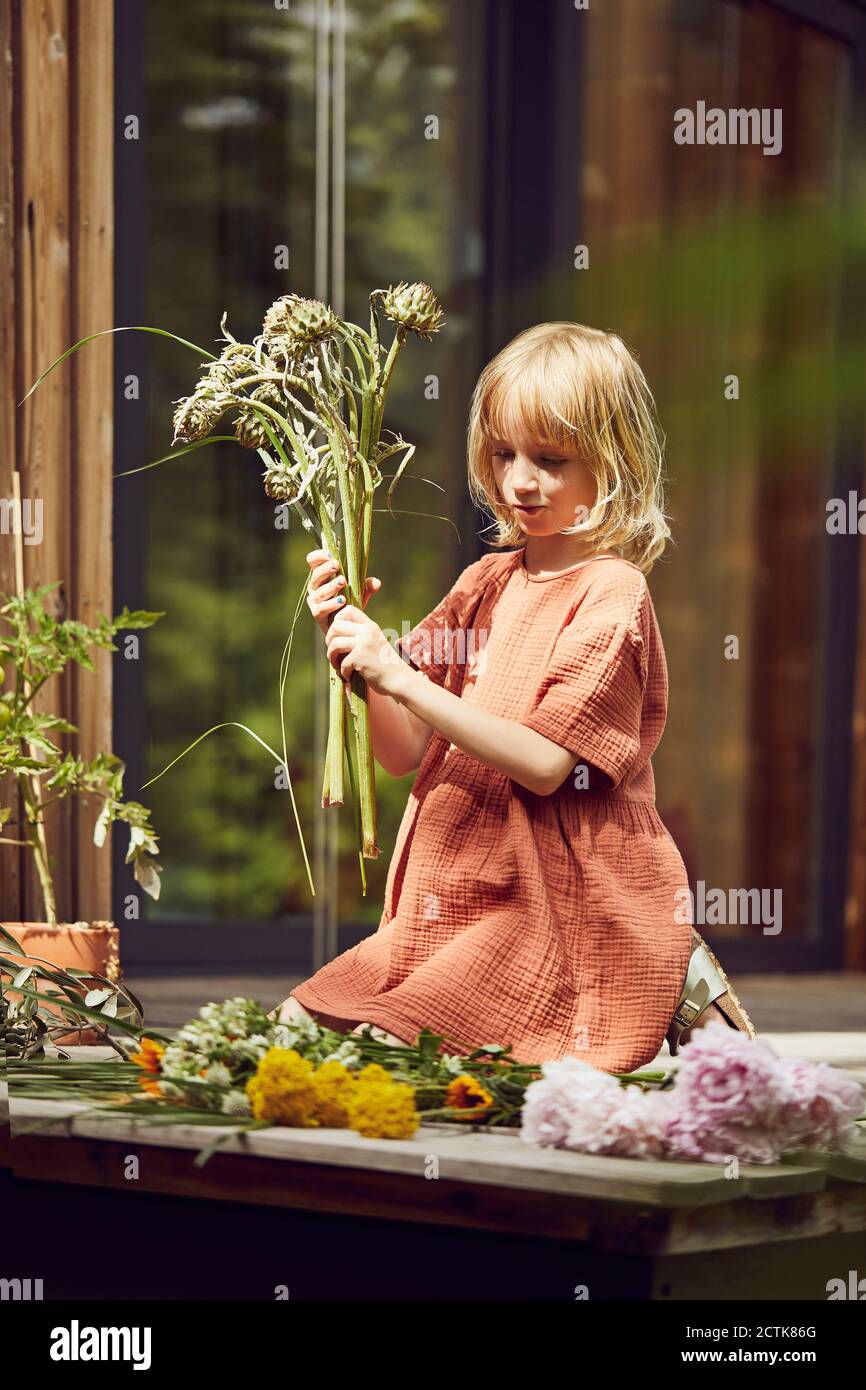 Girl arranging flowers while kneeling outside house at porch Stock Photo