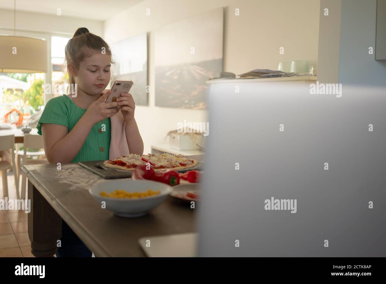 Girl taking photograph of pizza over kitchen island Stock Photo