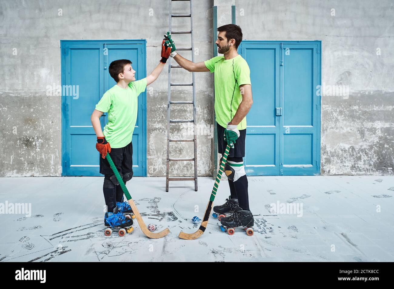 Father and son holding hockey sticks while giving high-fives against doors at court Stock Photo