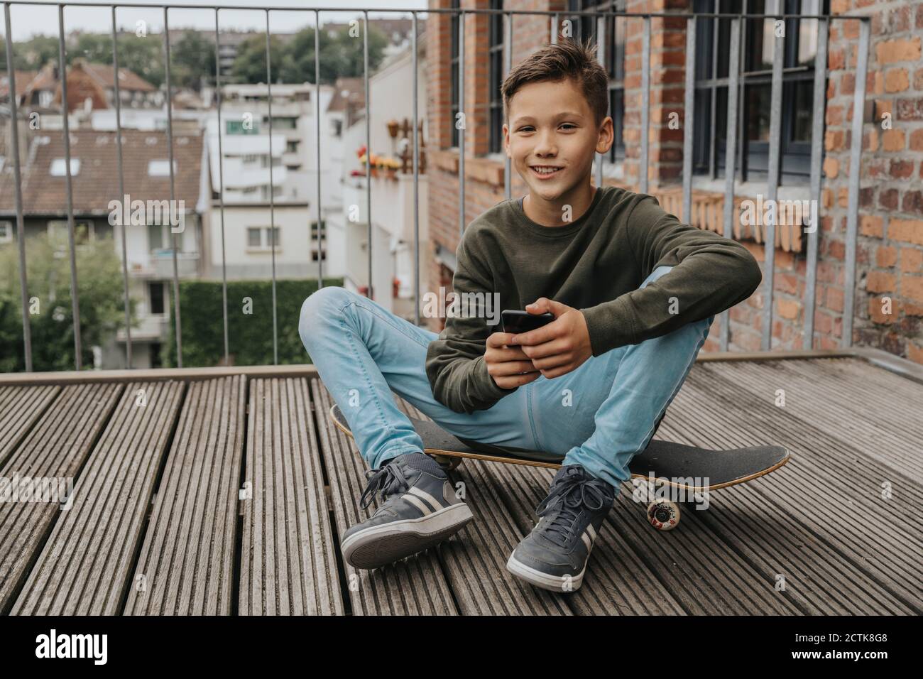 Smiling boy using smart phone while sitting on skateboard against railing Stock Photo