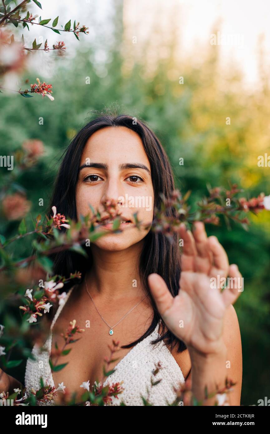 Young woman standing by flowering plant at public park Stock Photo