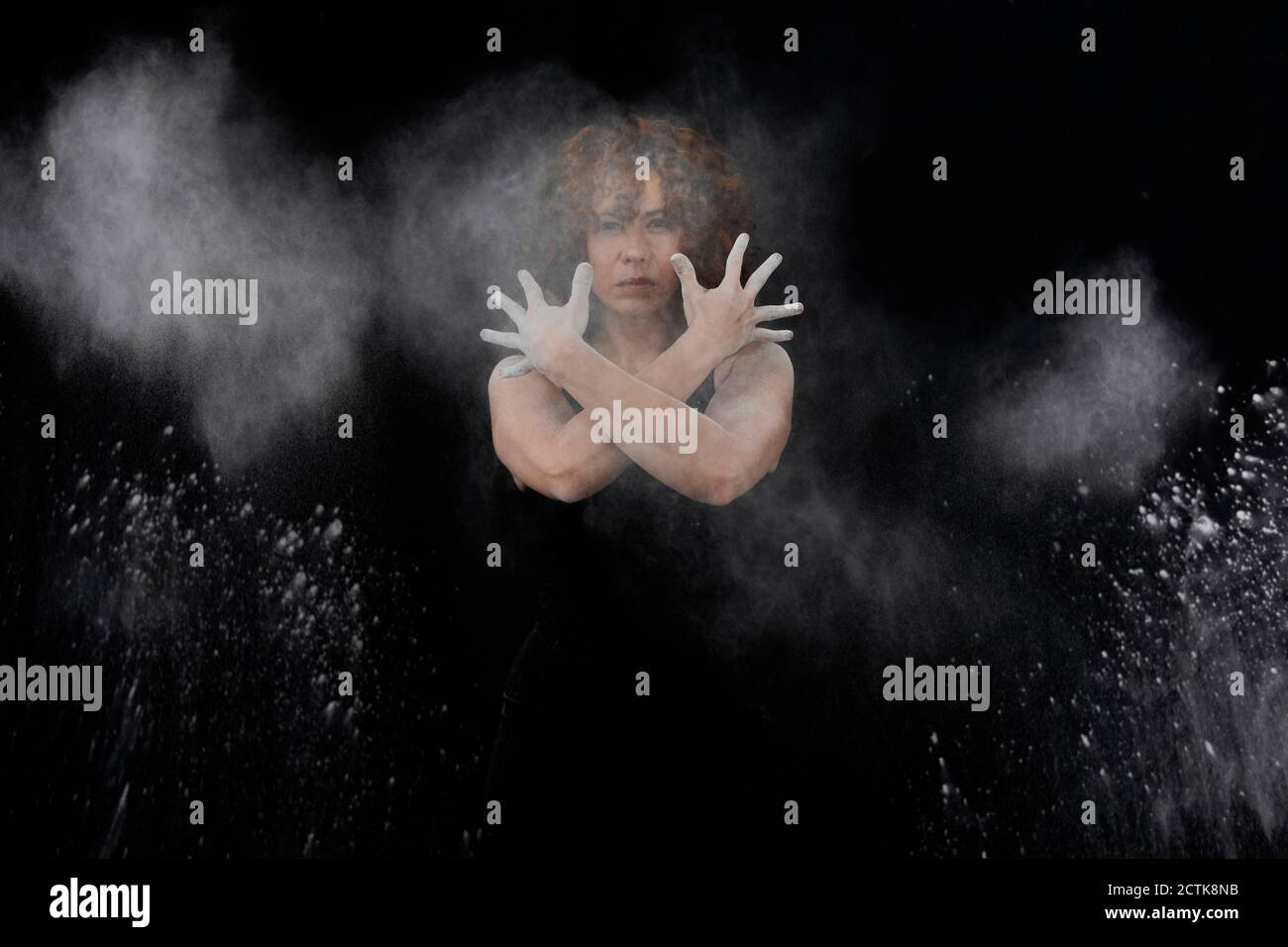 Woman throwing white dust besides herself while standing against black background Stock Photo
