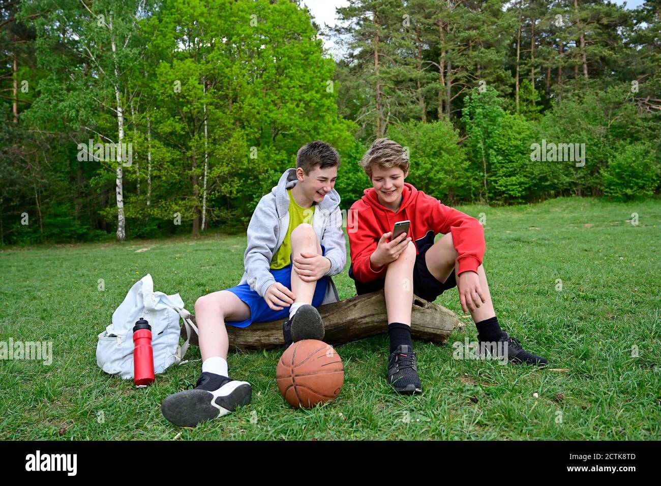 Smiling boys using mobile phone while sitting on log in forest Stock Photo