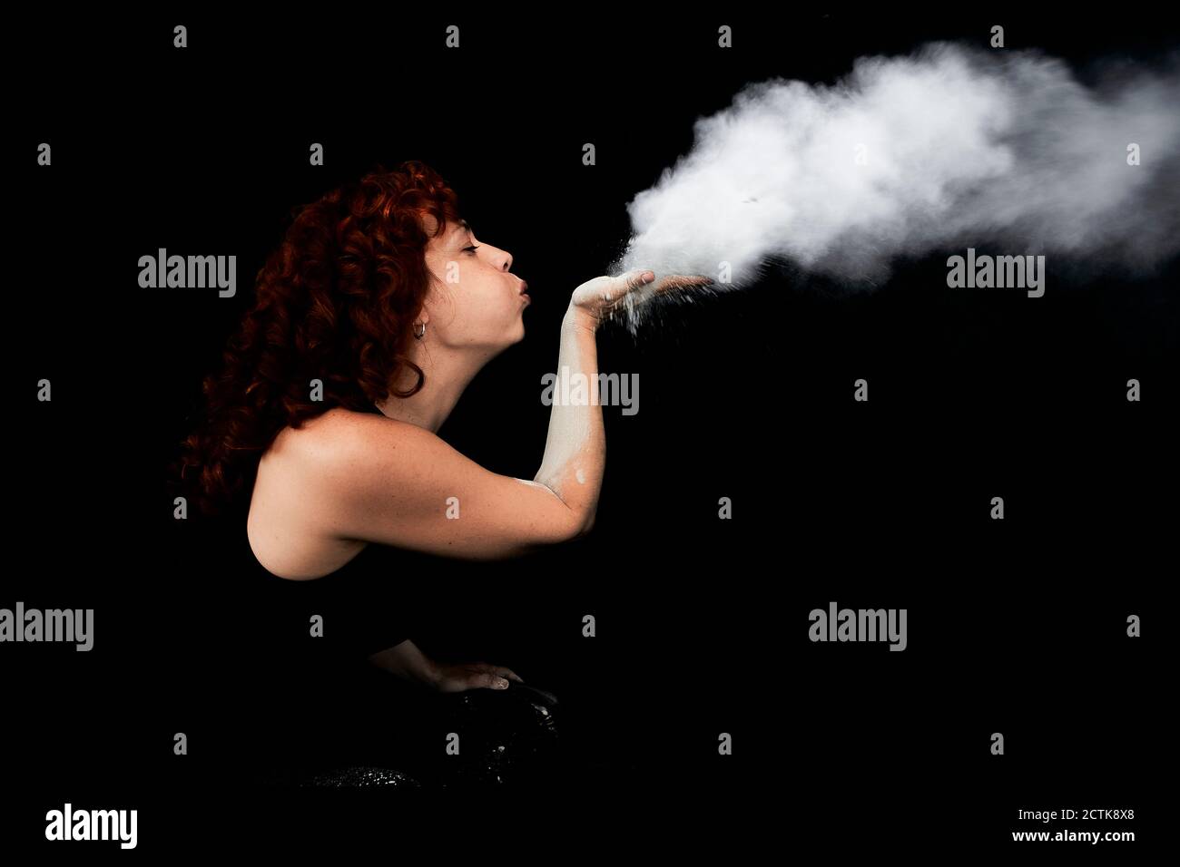 Woman blowing white dust while standing against black background Stock Photo
