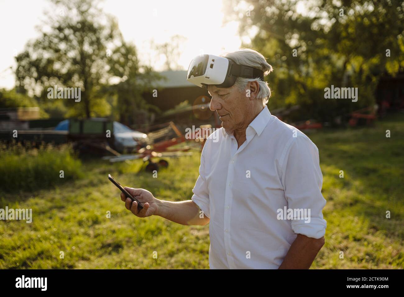 Man using phone while wearing VR glasses in backyard Stock Photo
