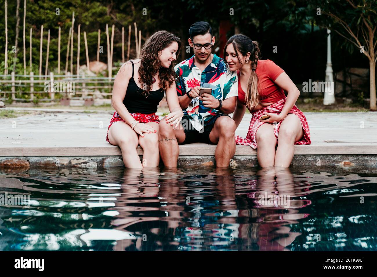 Friends using mobile phone while sitting at poolside Stock Photo