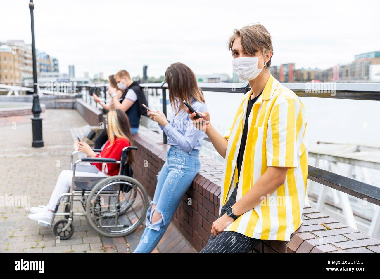 Young man keeping safe distance with friends while using mobile phones in city Stock Photo