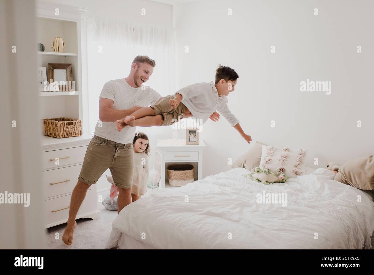 Playful father throwing son over bed while daughter standing in bedroom
