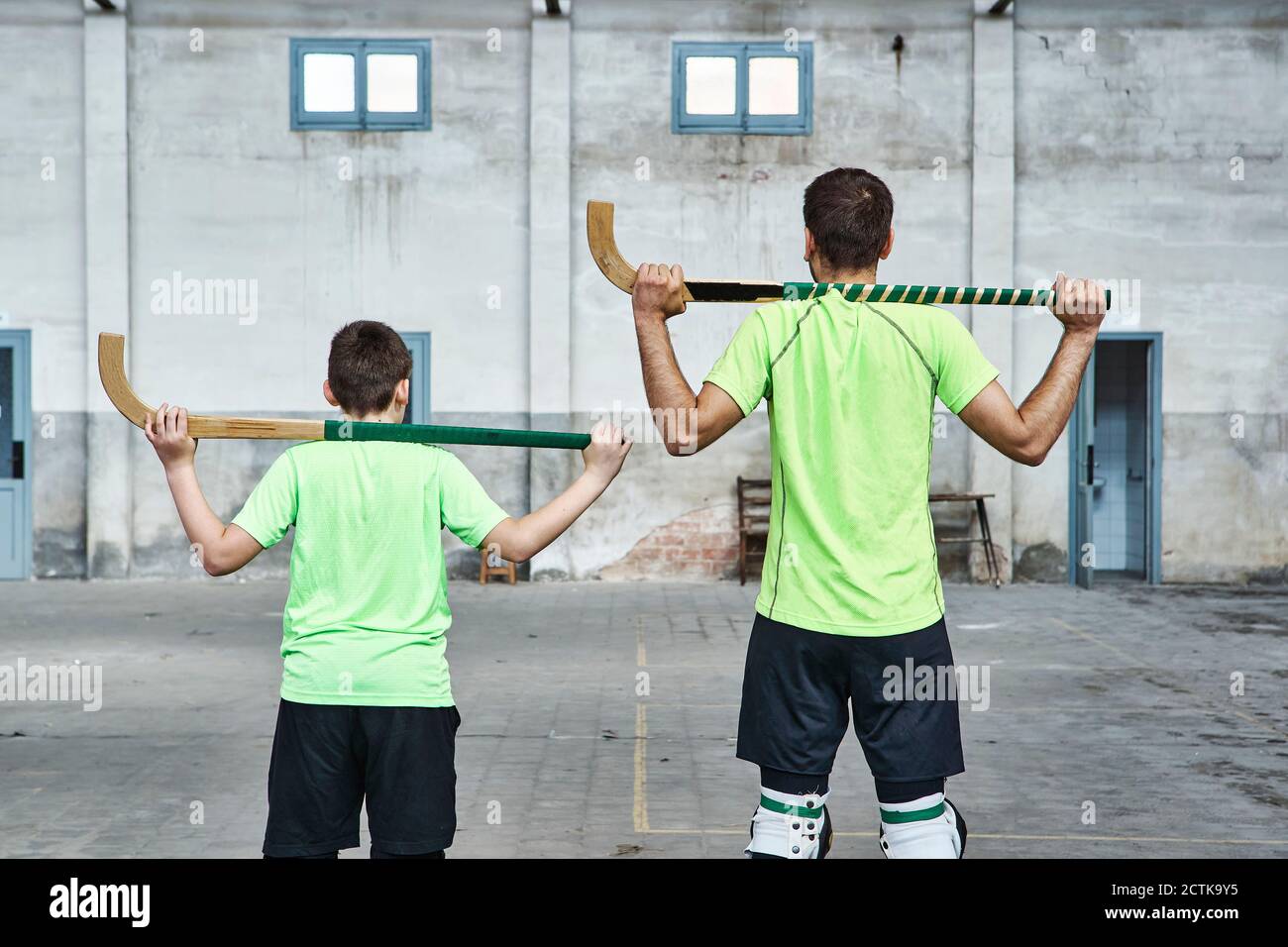 Father and son in uniform holding hockey sticks at sports court Stock