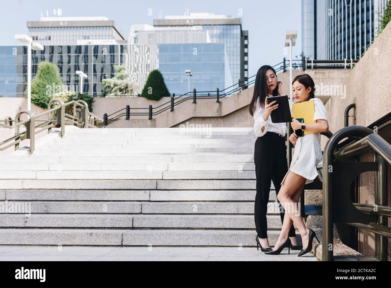 Female entrepreneurs standing on staircase against downtown district while using digital tablet Stock Photo