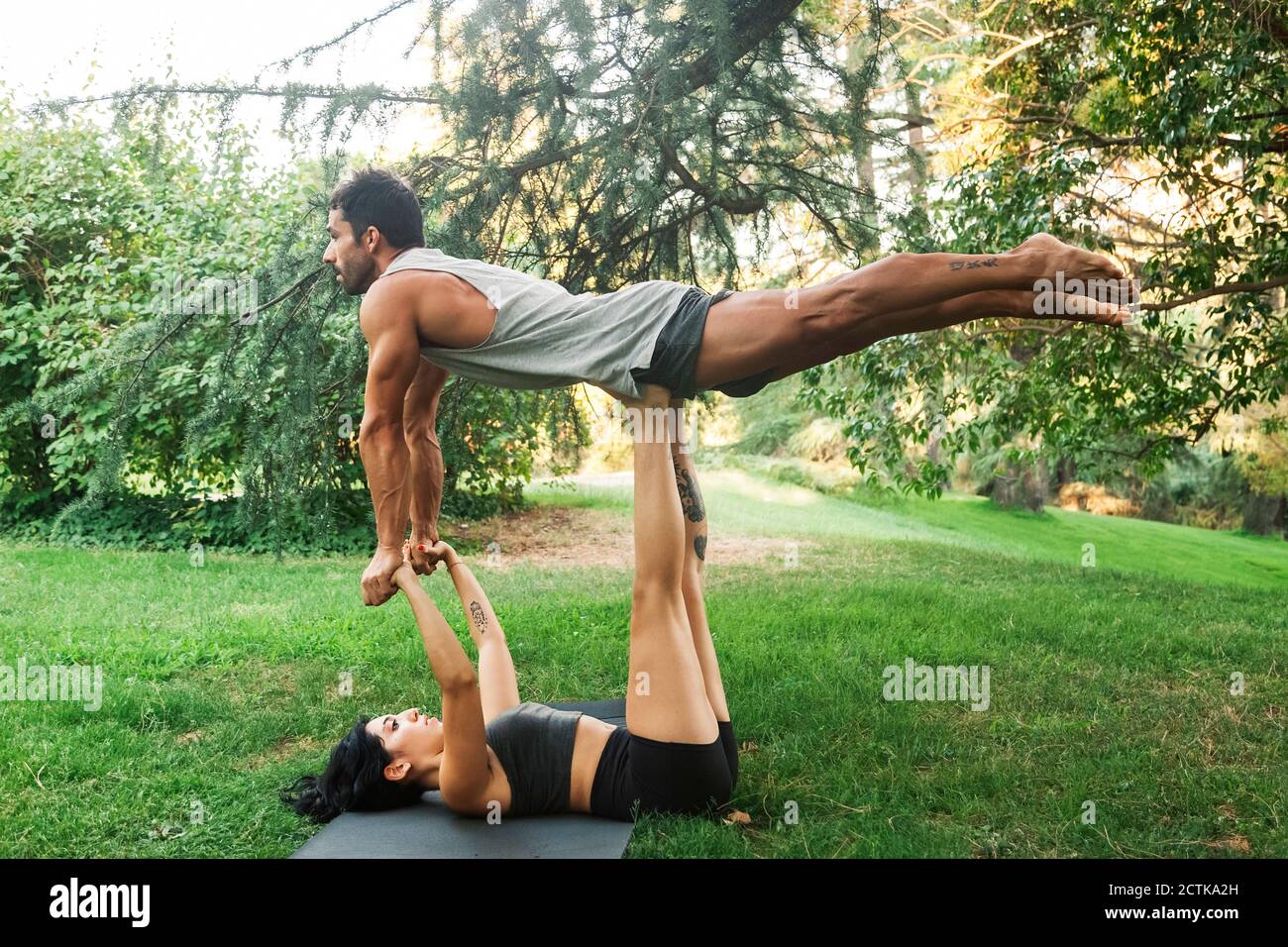 Female athlete balancing boyfriend on legs while holding hands in park Stock Photo