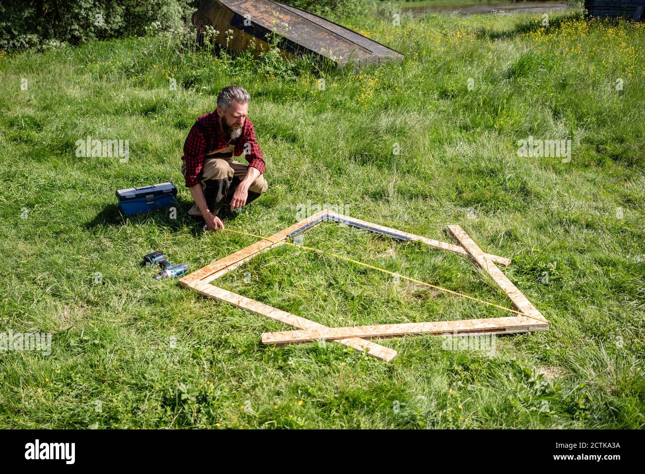 Carpenter crouching while measuring planks for playhouse on grass Stock ...
