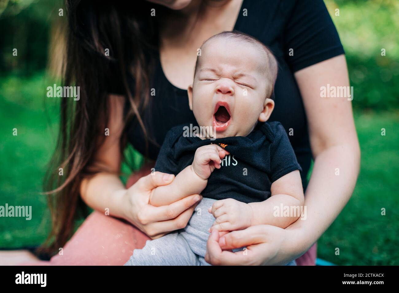Tired baby boy yawning while sitting with mother at park during weekend Stock Photo