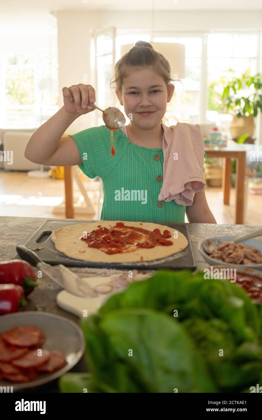 Cute smiling girl preparing pizza over kitchen island Stock Photo