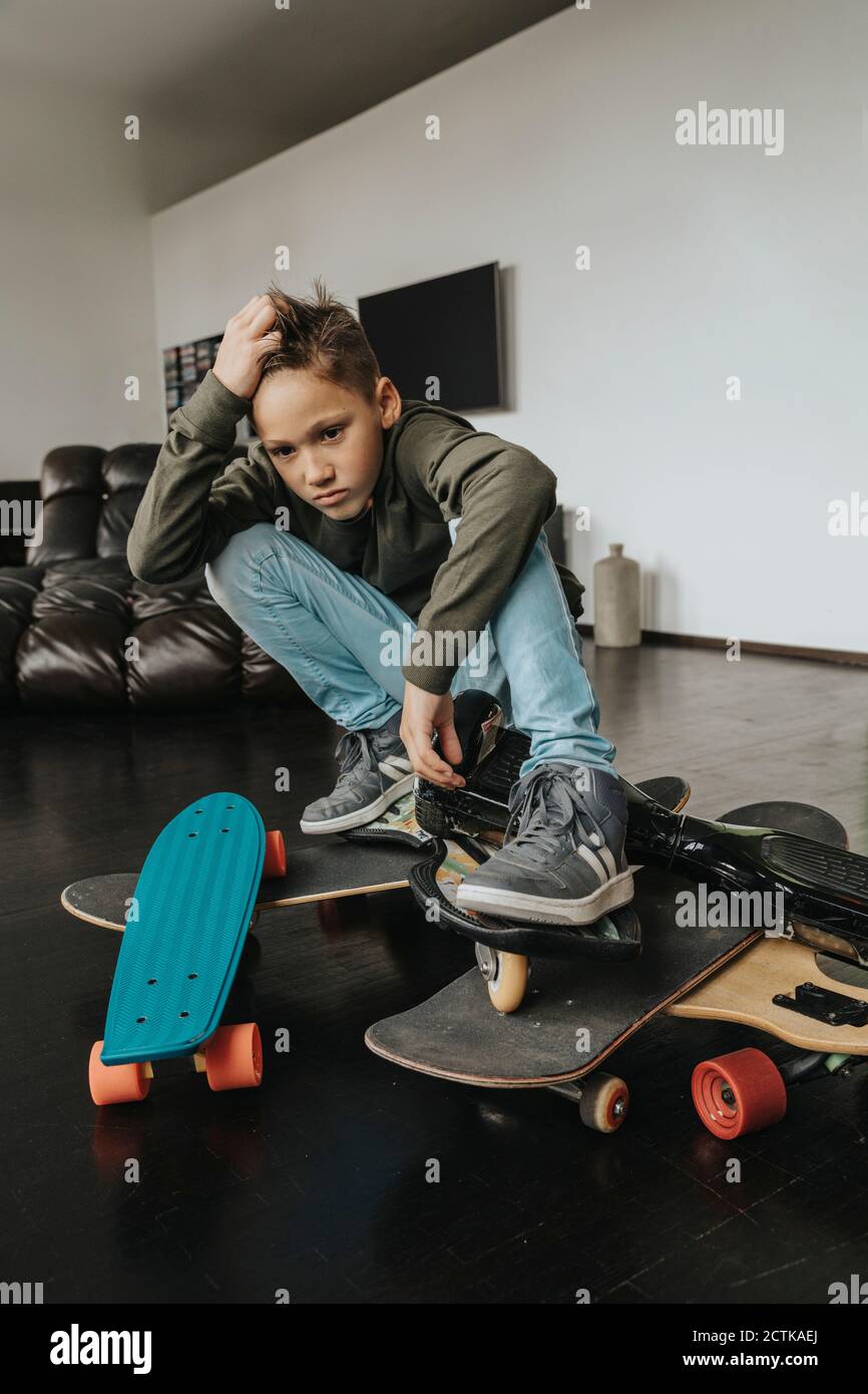 Confused boy with skateboards crouching on floor at home Stock Photo