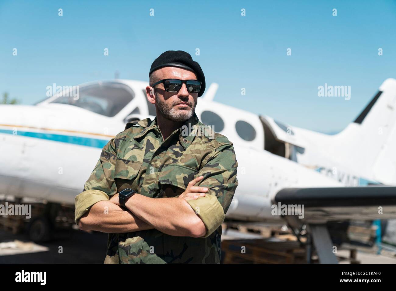 Confident army soldier standing with arms crossed against airplane on sunny day Stock Photo