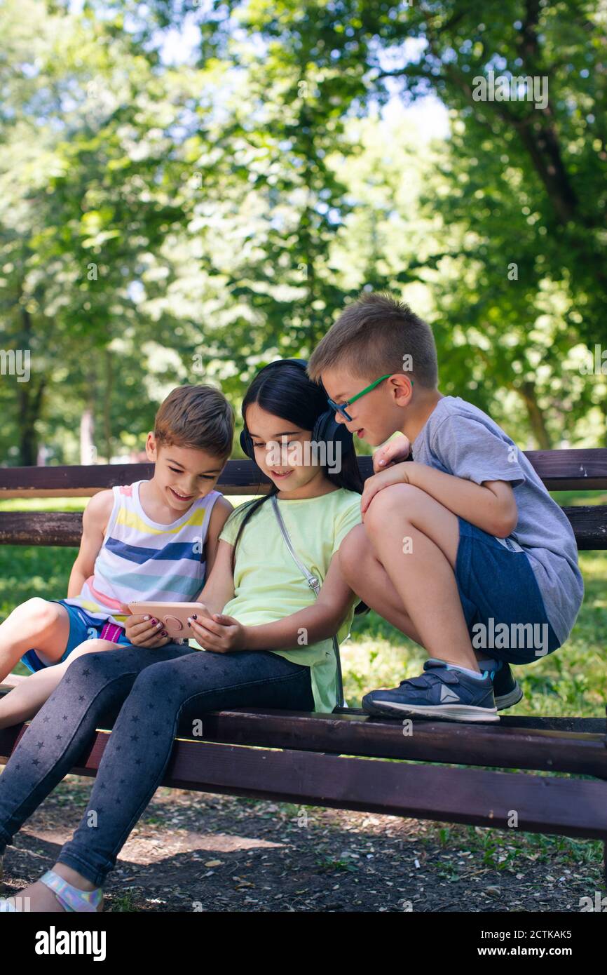 Girl wearing headphones showing technology to friends in park Stock Photo