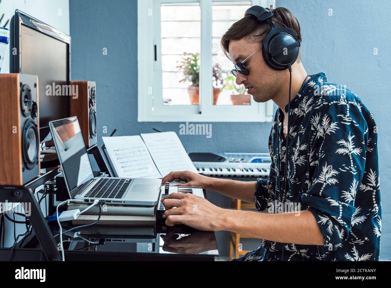 Man with headphones using laptop and keyboard at home Stock Photo