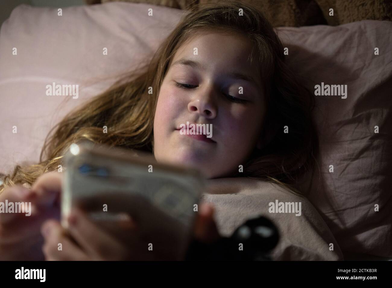 Girl using smart phone while lying in bedroom Stock Photo