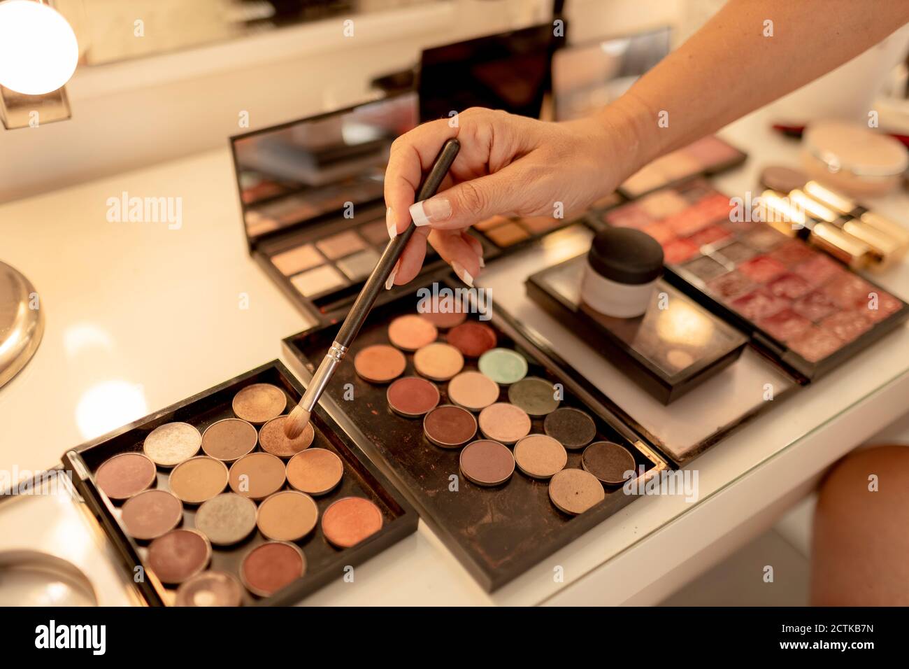 Close-up of beautician's hand with make-up brush and palettes on dressing table Stock Photo