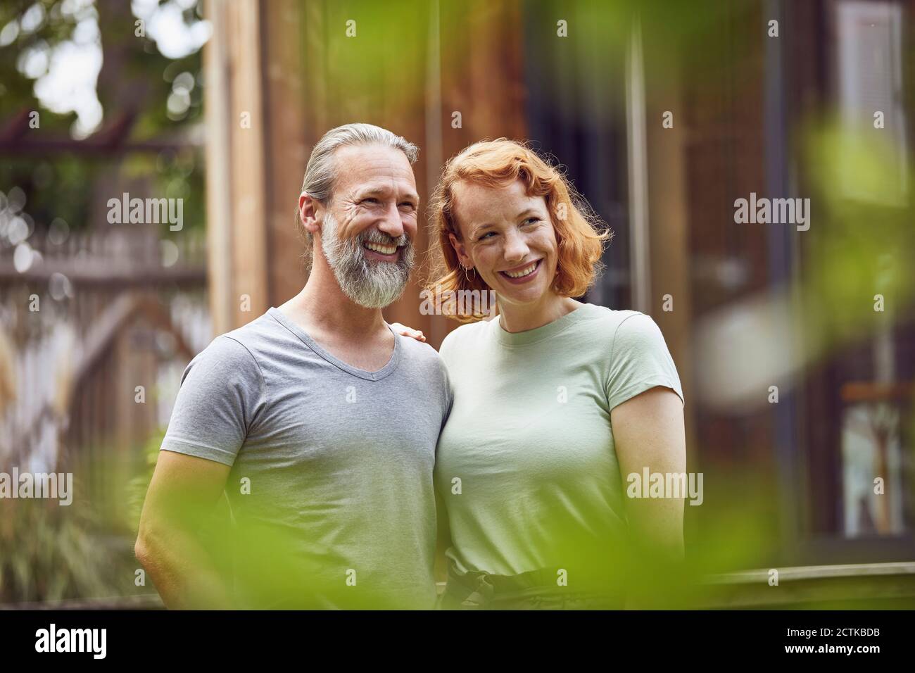 Smiling couple looking away while standing against tiny house in yard Stock Photo