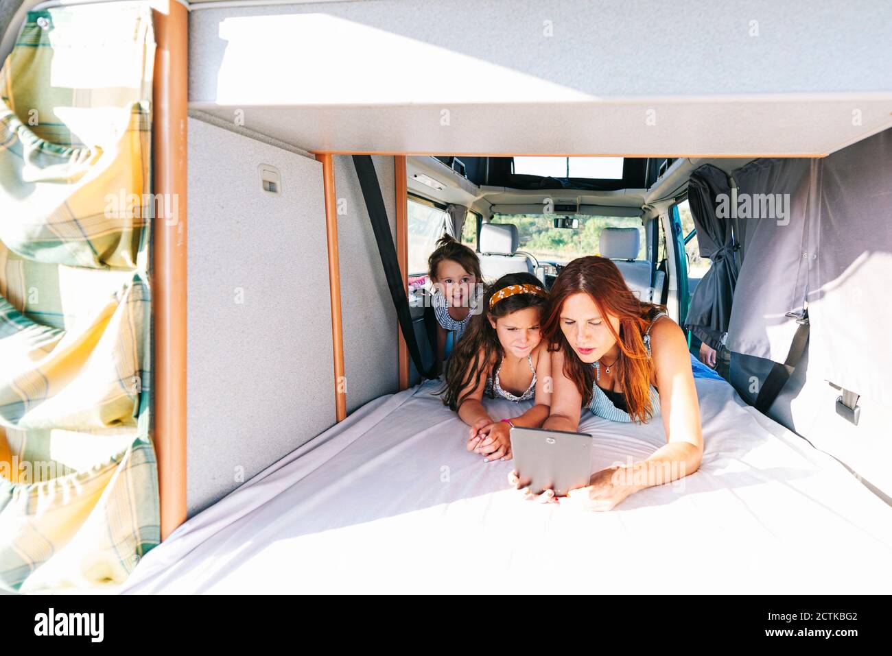 Mother with daughters using digital tablet while lying on bed in motor home Stock Photo