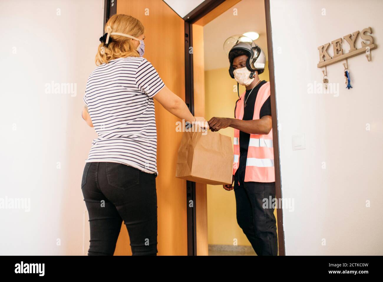 Woman taking paper bag from delivery man with protective mask Stock ...