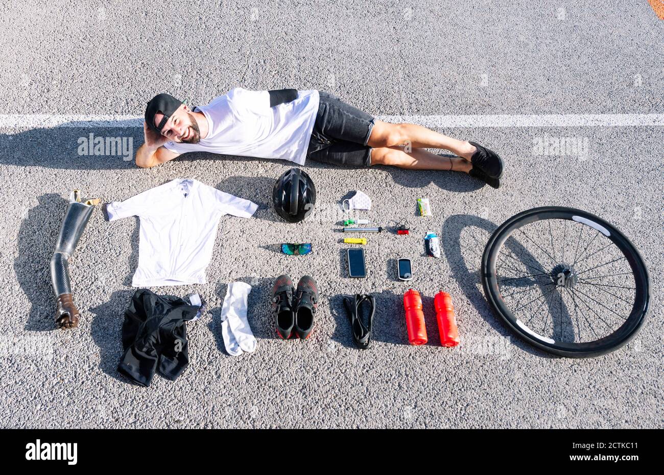 Smiling male adaptive athlete with various objects lying on road Stock Photo