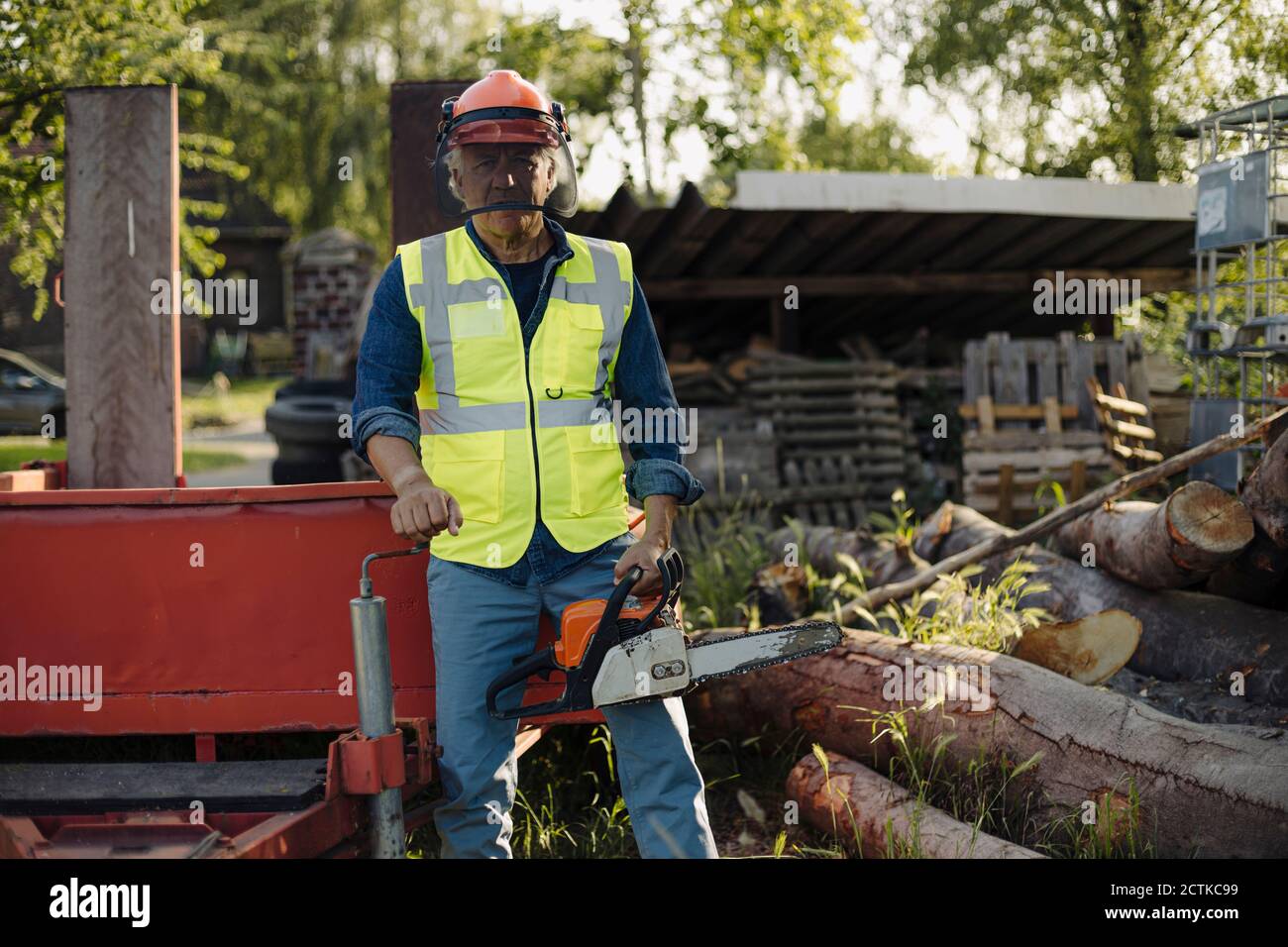 Man holding chainsaw while standing by log in forest Stock Photo